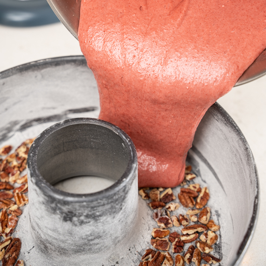 Pouring cake batter over the crushed pecans in the bundt pan