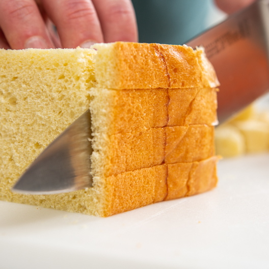 Bread being sliced into pieces for bread pudding